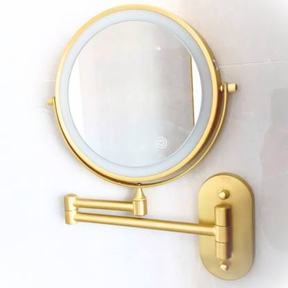 Gold wall-mounted makeup mirror with light on a white background