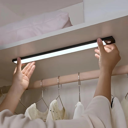 Josh & Tate - GlowMotion Motion Sensor Lamp - Person installing a LED strip light under a bed with clothes hanging below.