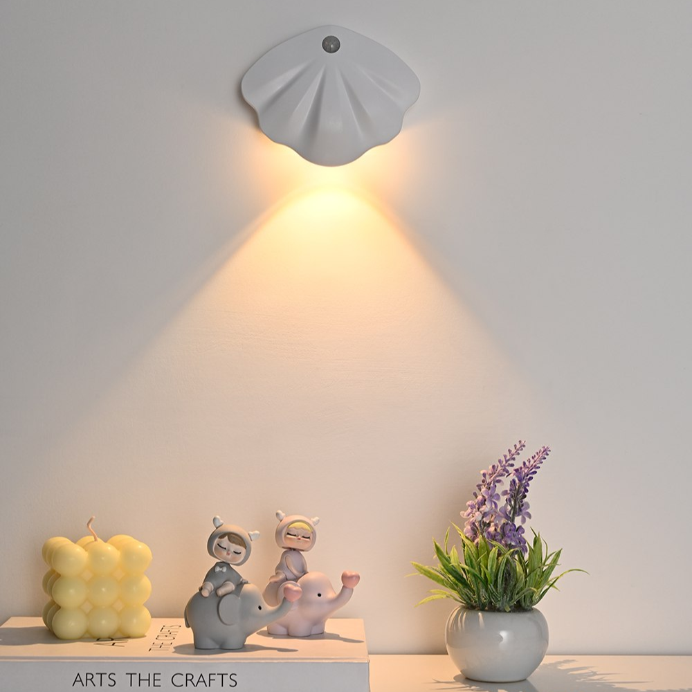 Wall-mounted shell-shaped light fixture casting a warm glow on a neutral background with decorative items below.