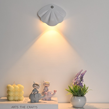 Wall-mounted shell-shaped light fixture casting a warm glow on a neutral background with decorative items below.