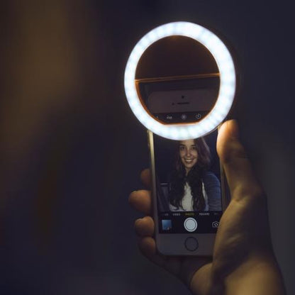 Hand holding a smartphone with a ring light in a dark setting