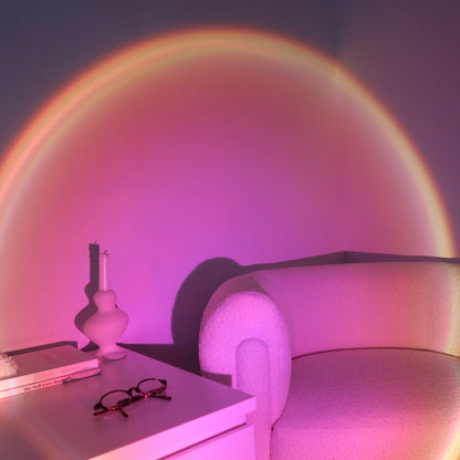 Room with a rainbow light projection on the wall, featuring a white nightstand and chair.