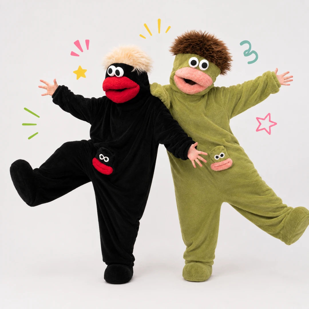 Josh & Tate - GoofSuit™ Big Mouth Monster Onesie - Two children wearing plush monster costume jumpsuits pose together against a light gray studio background. One costume is black with a red mouth and beige hair, and the other is olive green with a pink mouth and brown hair.