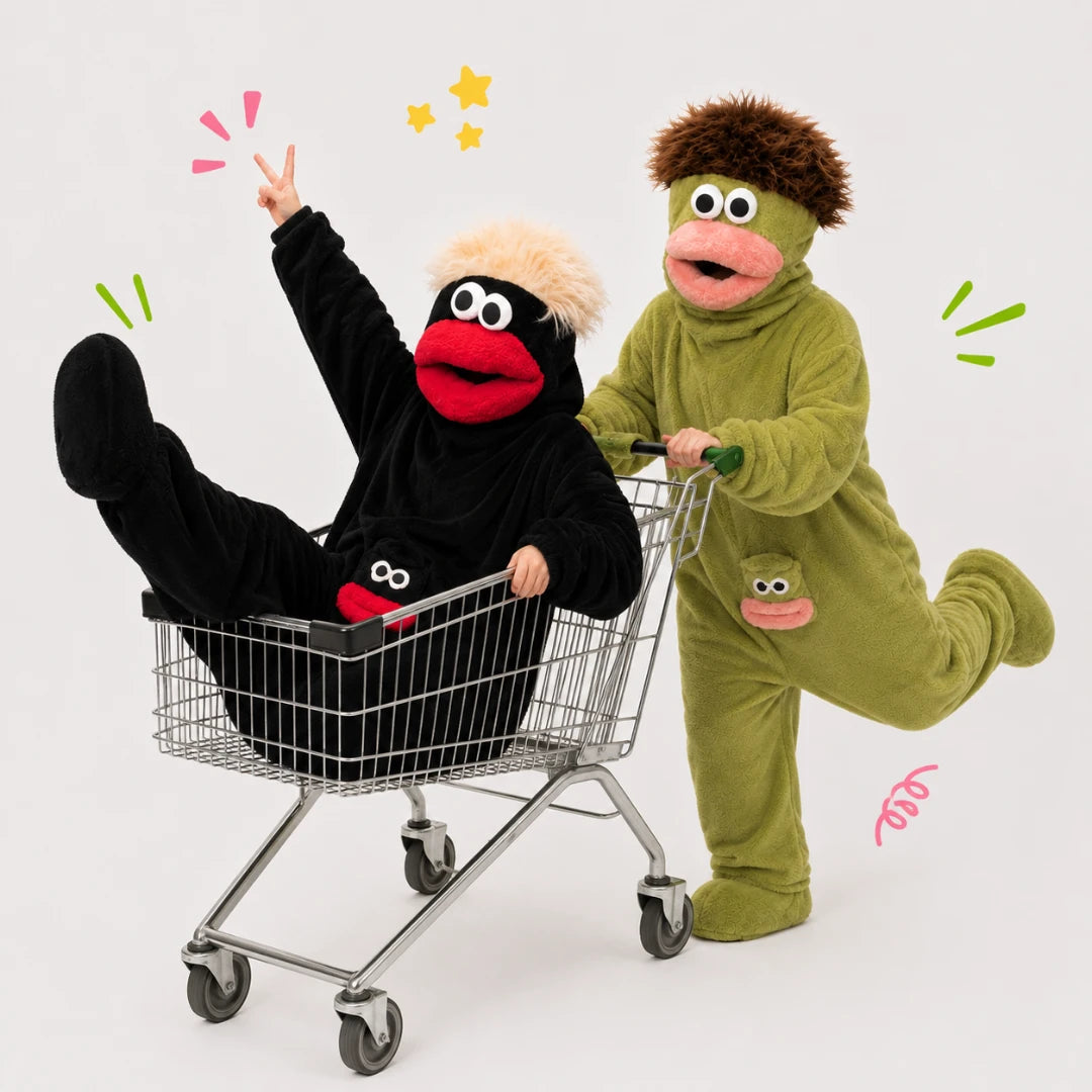 Josh & Tate - GoofSuit™ Big Mouth Monster Onesie - Two people in costume posing with a shopping cart on a light gray studio background. One person wears a black plush monster costume with a red mouth and raised arm, reclining in the cart.