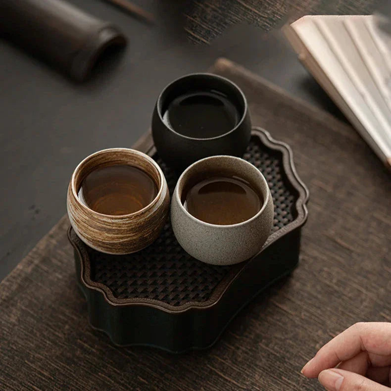 Set of ceramic cups on a dark wooden tray with a hand reaching in