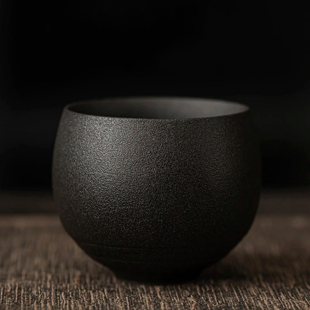 Black textured ceramic cup on a wooden surface with a dark background