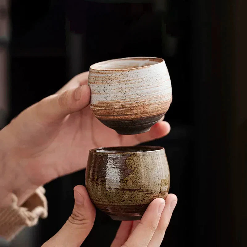 Two hands holding ceramic cups against a dark background
