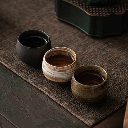 Three ceramic cups on a wooden surface with a woven mat