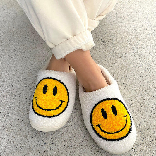 White slippers with yellow smiley face design worn by a person on a light gray floor.