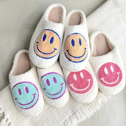 Pair of white slippers with colorful smiley face designs on a textured surface.