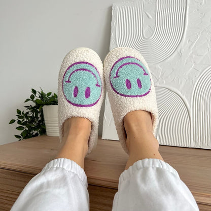 White slippers with smiley face design worn indoors on a wooden surface.