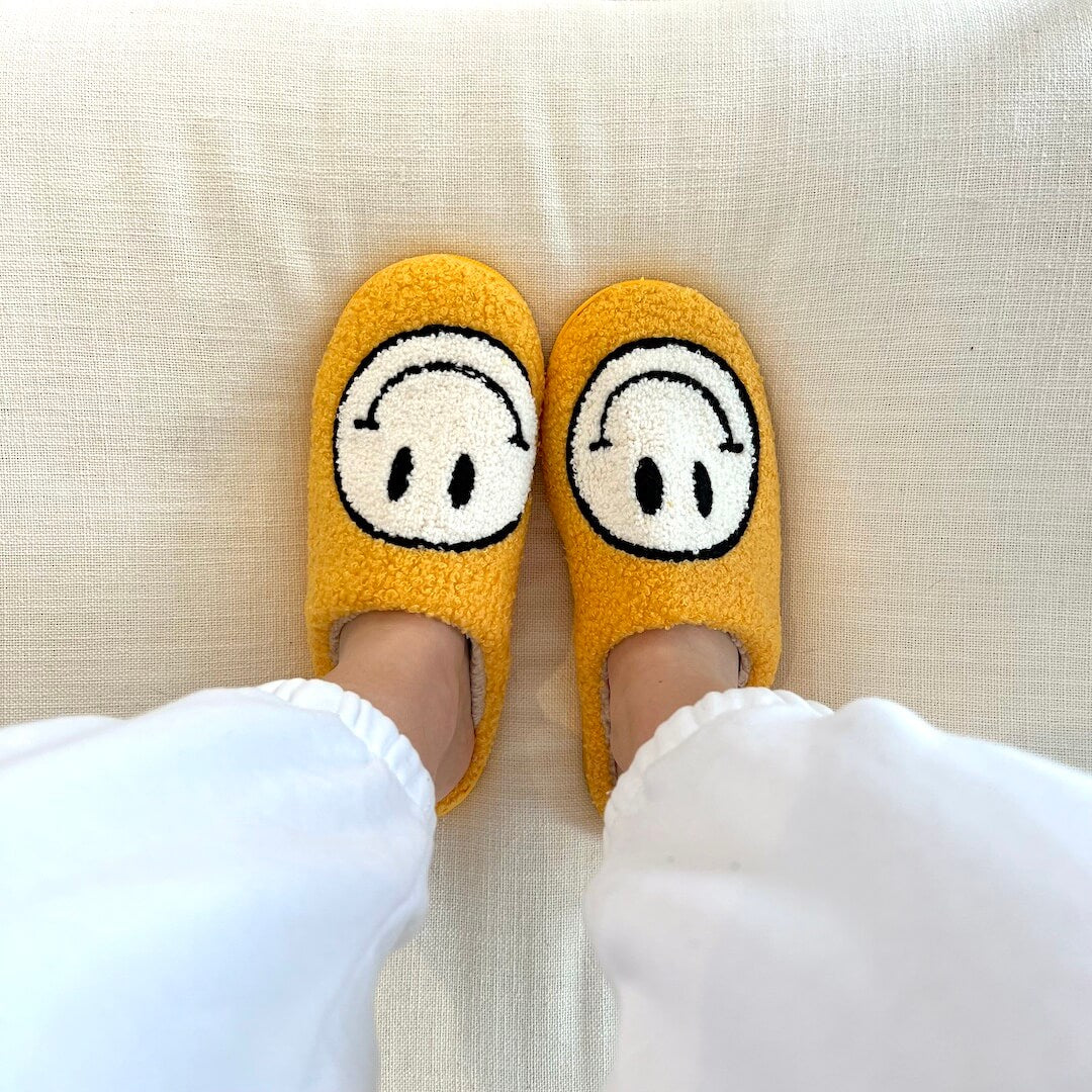Yellow slippers with cartoon face design worn on a light-colored couch.