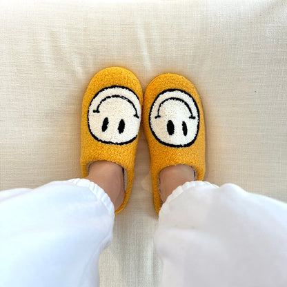 Yellow slippers with cartoon face design worn on a light-colored couch.