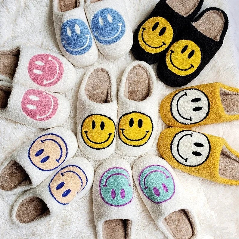 Smiley face slippers in various colors arranged on a soft surface.