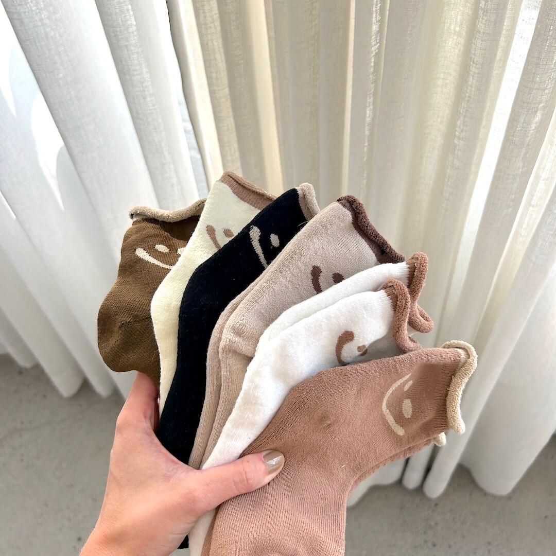 Hand holding a set of patterned socks in front of white curtains