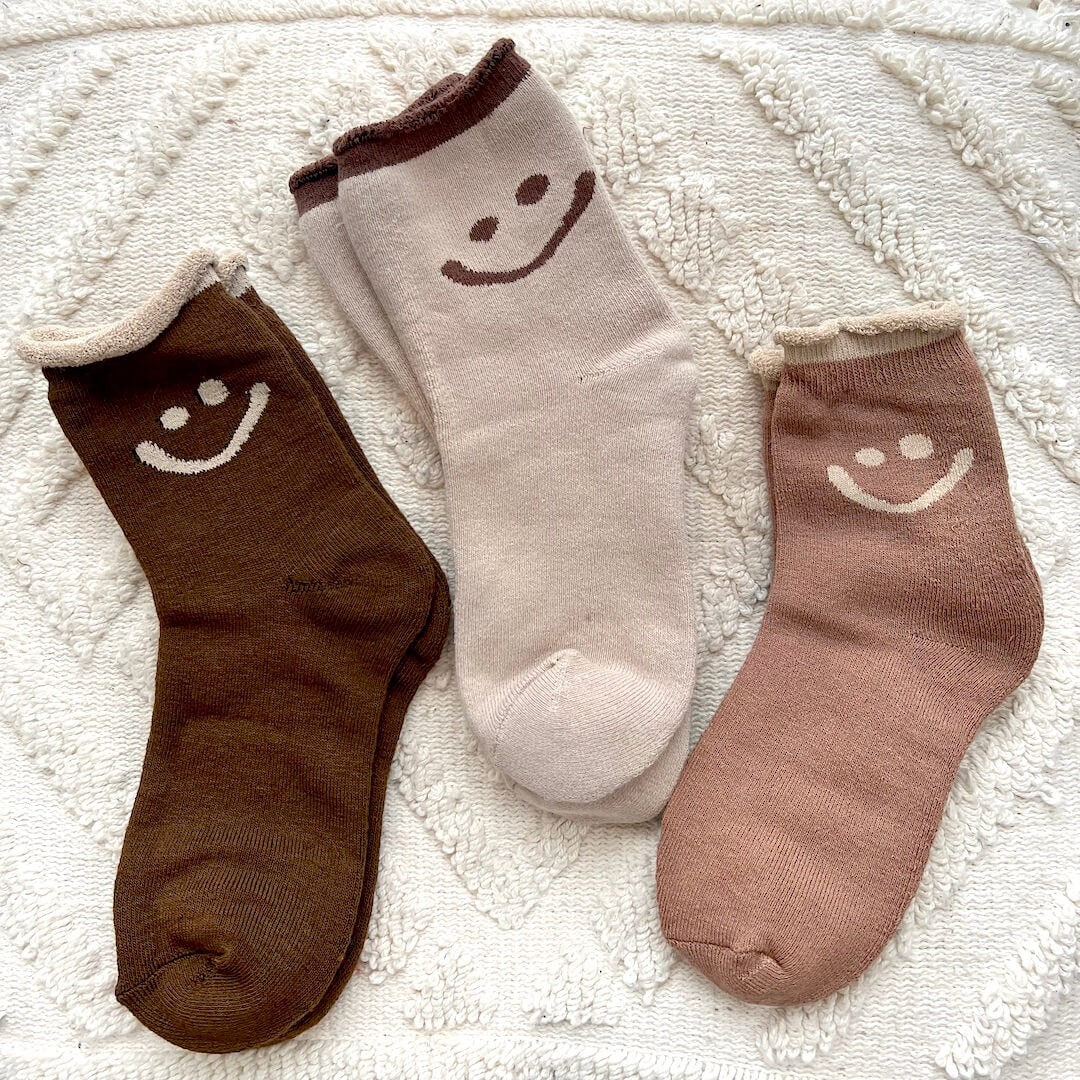 Three socks with smiley face designs on a textured white surface