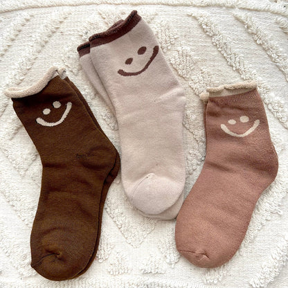Three socks with smiley face designs on a textured white surface