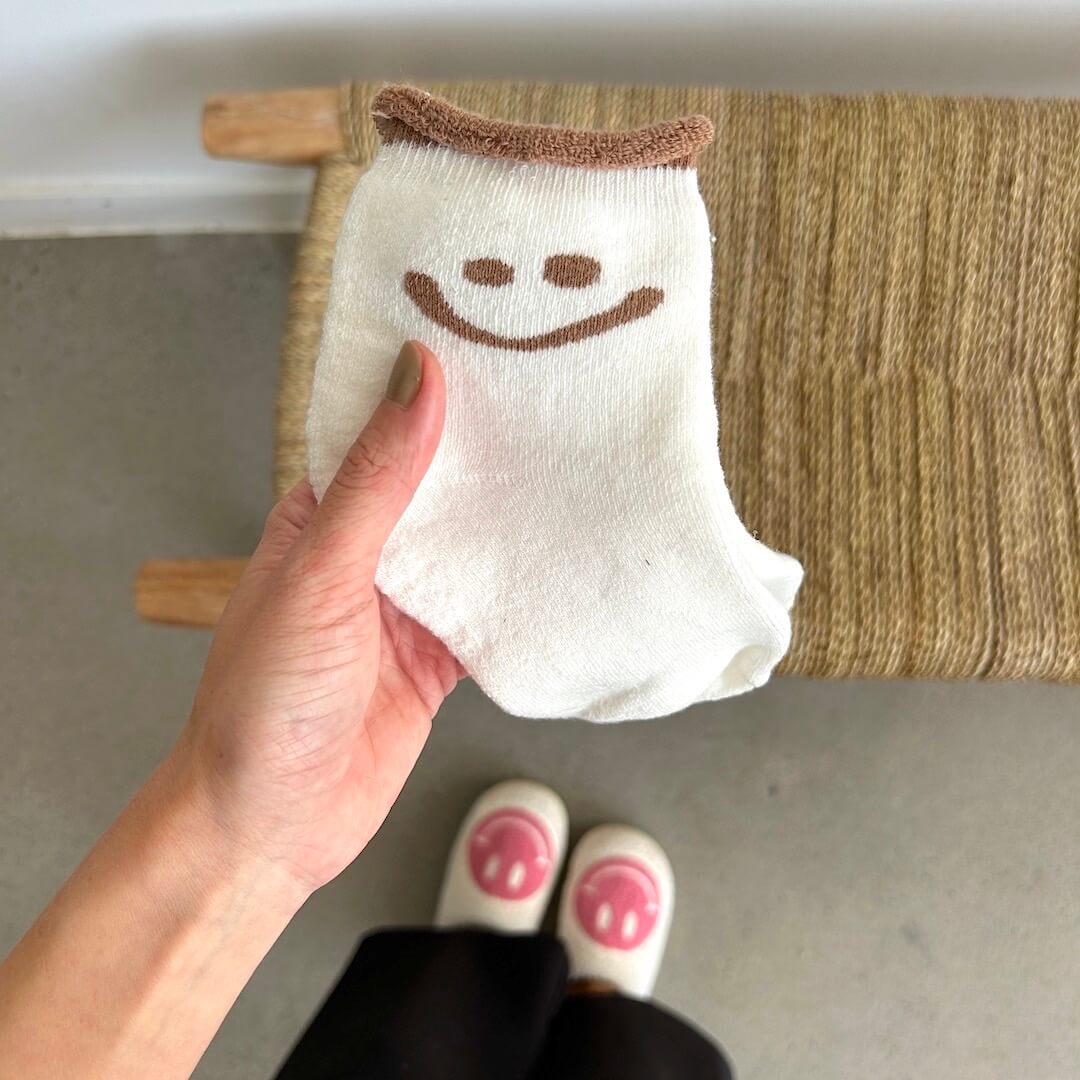 Hand holding a white sock with a smiley face design against a neutral background