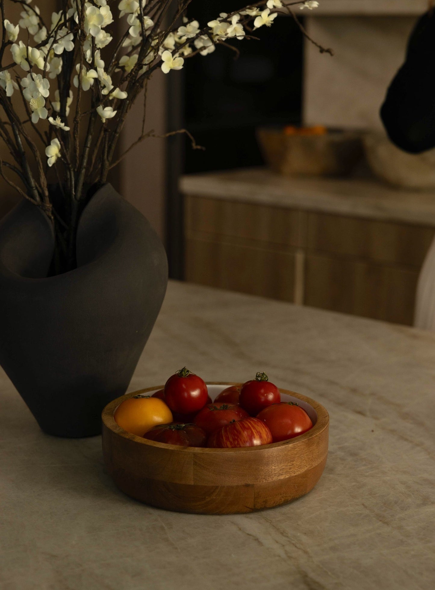 Wooden bowl with fruits on a table next to a vase with white flowers