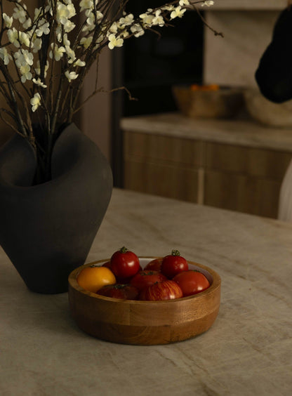 Wooden bowl with fruits on a table next to a vase with white flowers