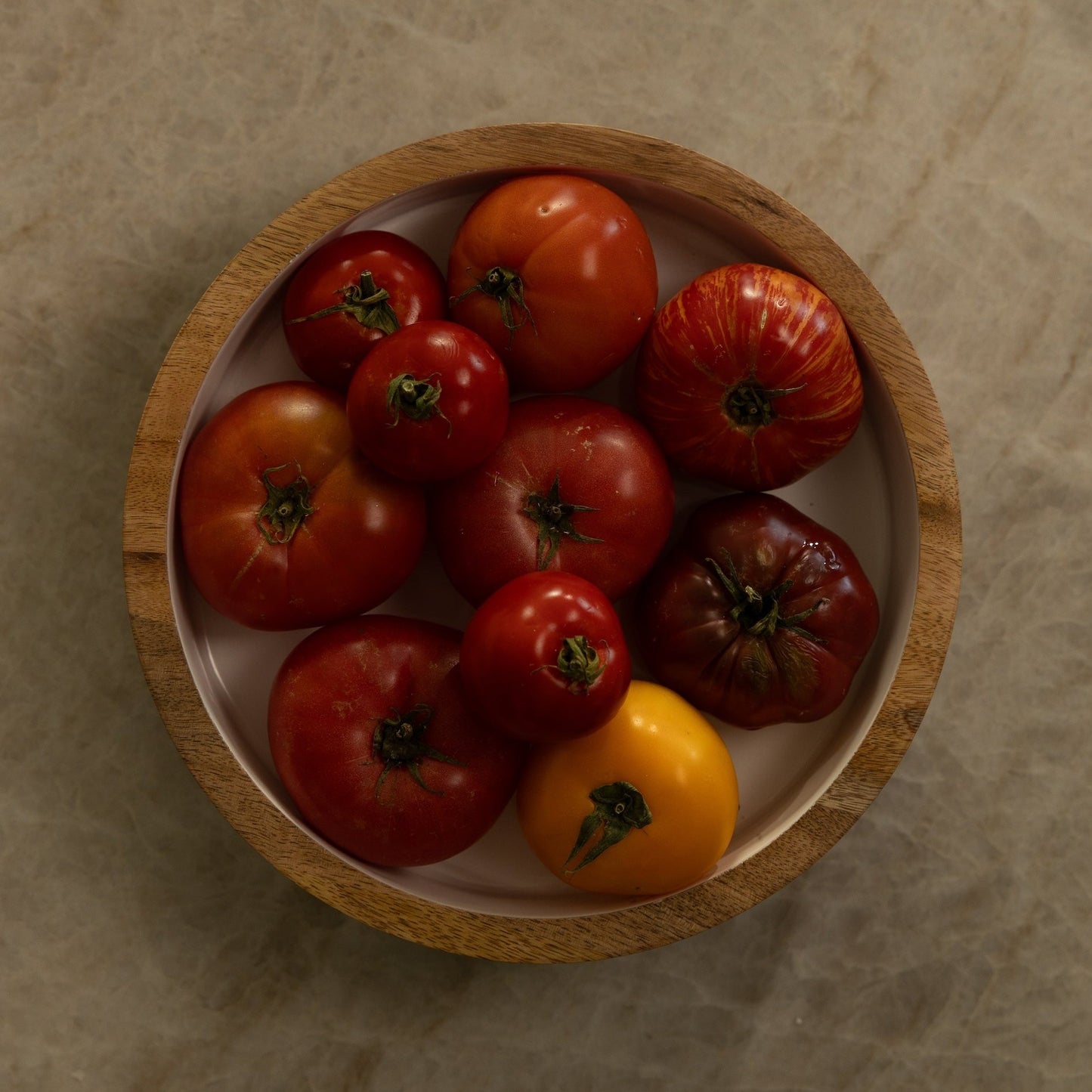 Wooden bowl with red and yellow tomatoes on a beige surface