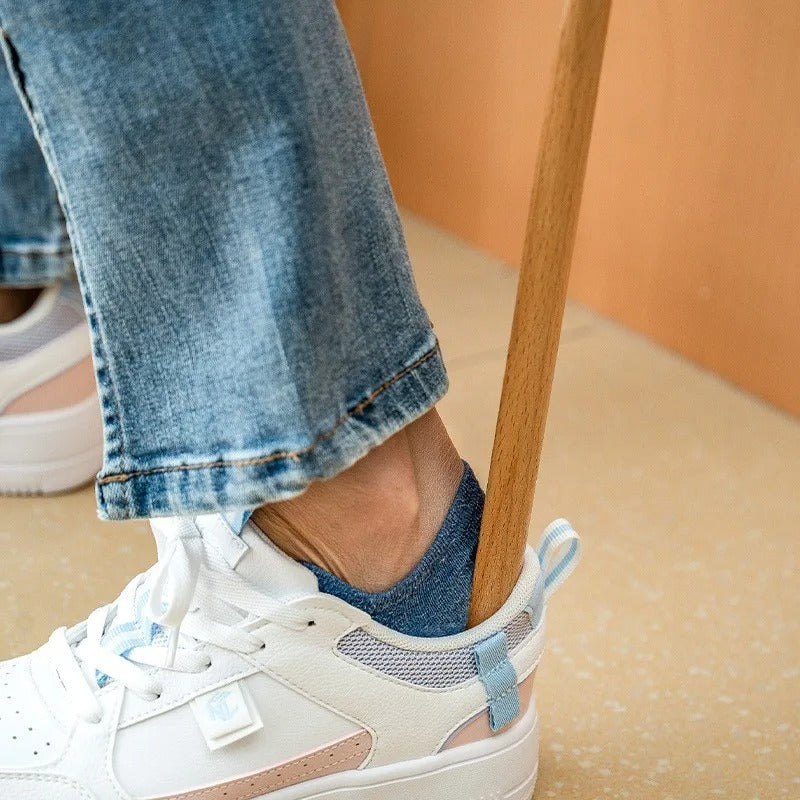 Person wearing white sneakers with blue accents and rolled-up jeans against a peach-colored wall.