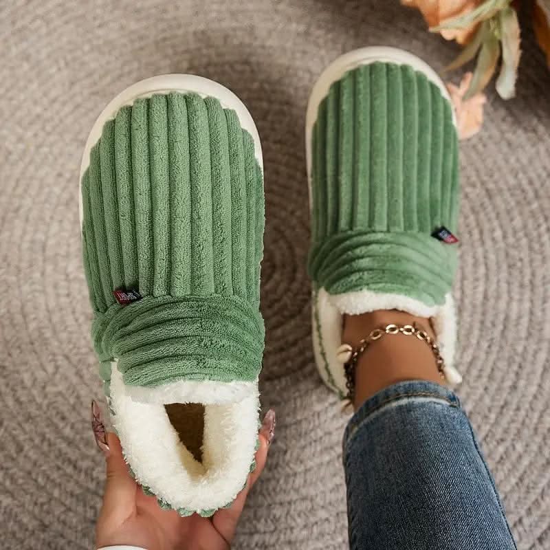 Green slippers with white soles worn indoors on a textured floor.