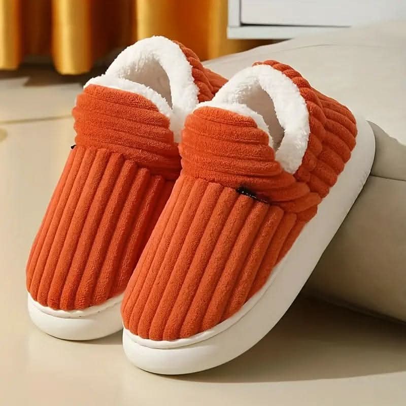 Pair of orange slippers with white soles on a light surface.