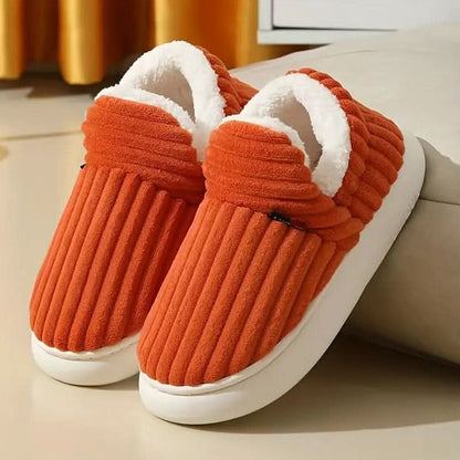 Pair of orange slippers with white soles on a light surface.