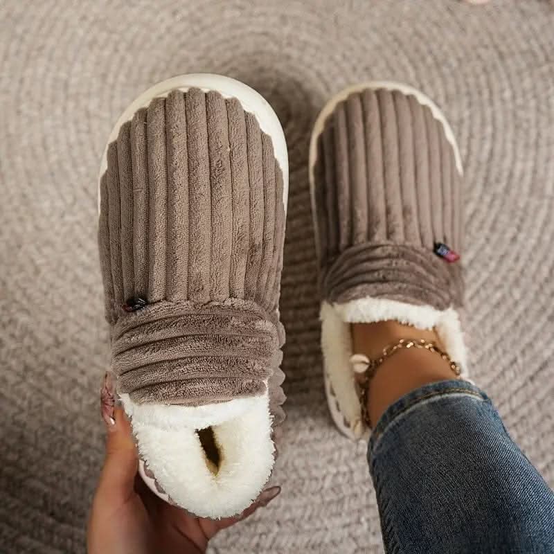 Brown slippers with white soles worn indoors on a textured floor.