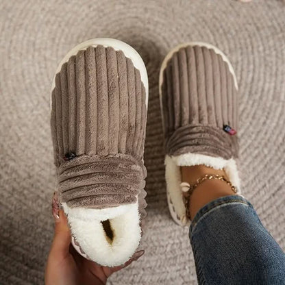 Brown slippers with white soles worn indoors on a textured floor.