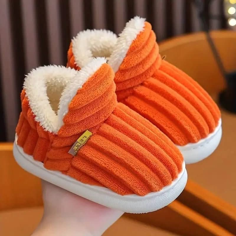 Orange slippers with white lining held by a person indoors.