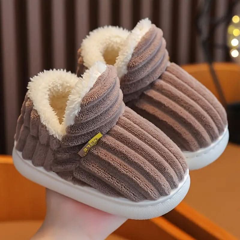 Brown plush slippers held in a hand with a blurred background