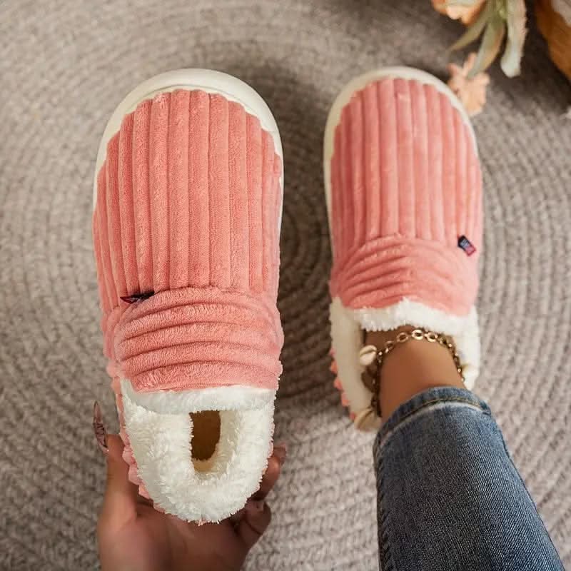 Pink slippers with white soles worn by a person on a textured surface