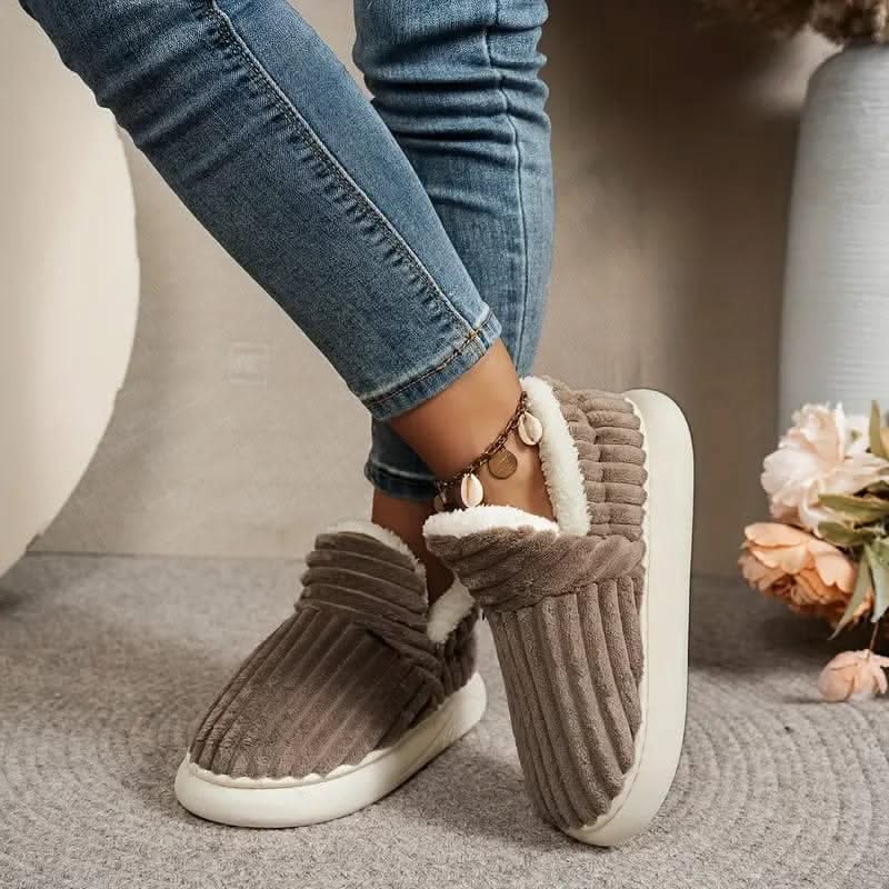 Brown slippers with white soles worn with blue jeans on a neutral background