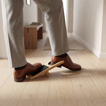 Josh & Tate - HeelHook™ Wooden Boot Jack - Person using a wooden footrest on a light wood floor.
