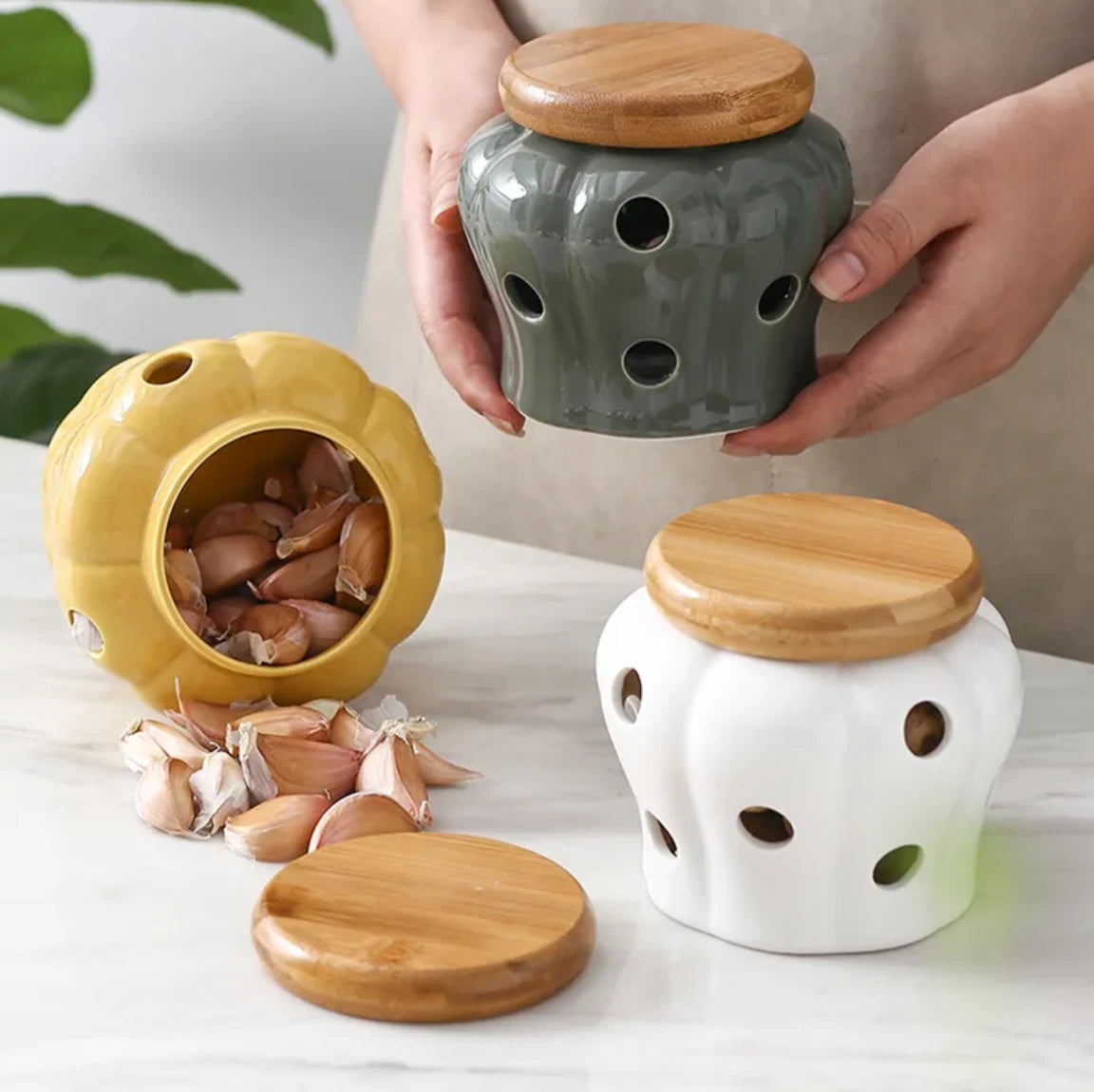 Three ceramic containers with wooden lids on a light surface, surrounded by garlic bulbs.