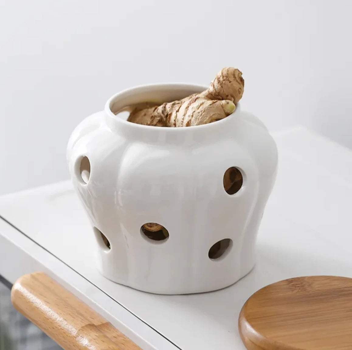 White ceramic pot with holes containing ginger on a white surface.