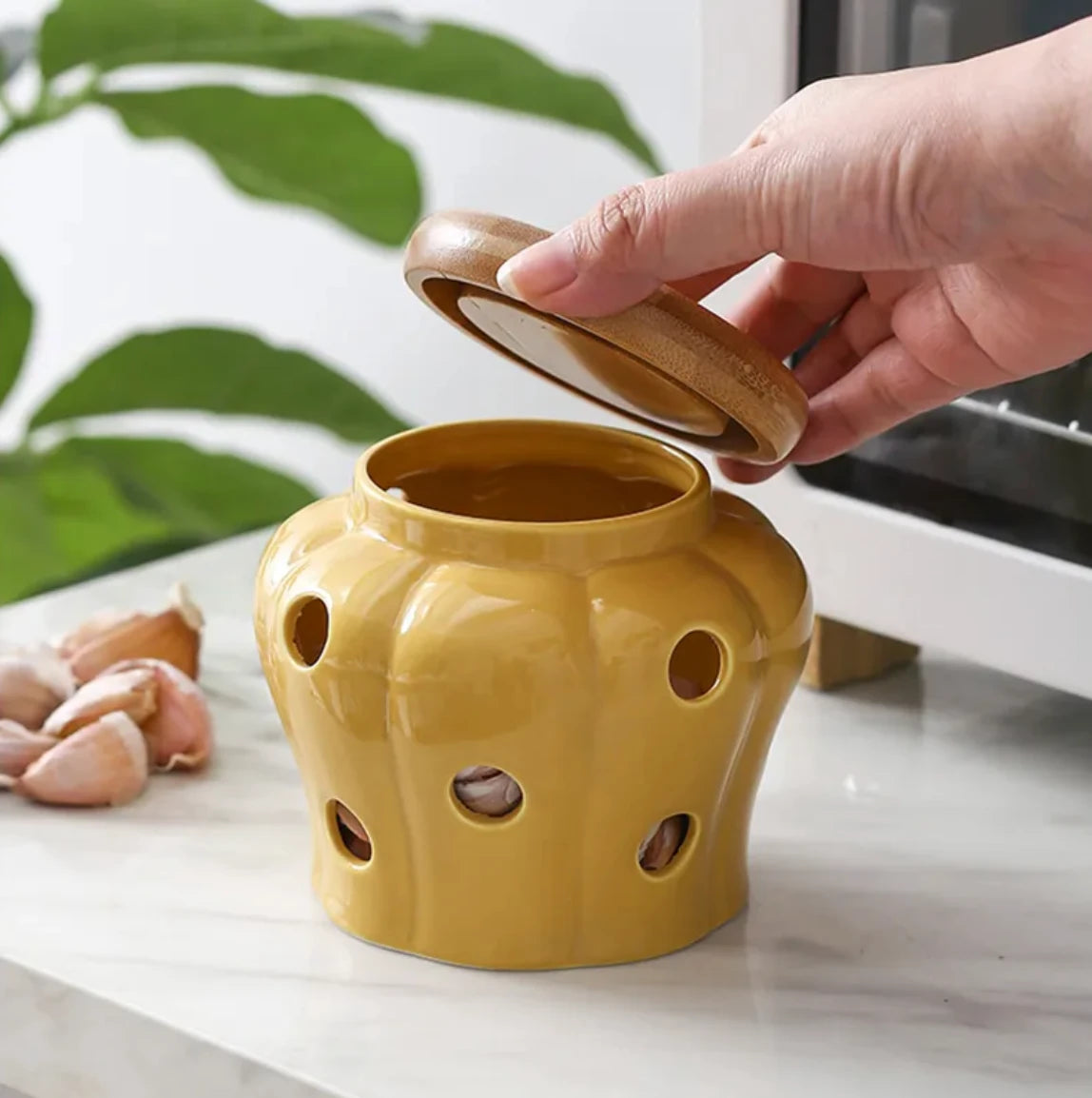 Yellow ceramic container with holes on a white surface, hand holding a lid.