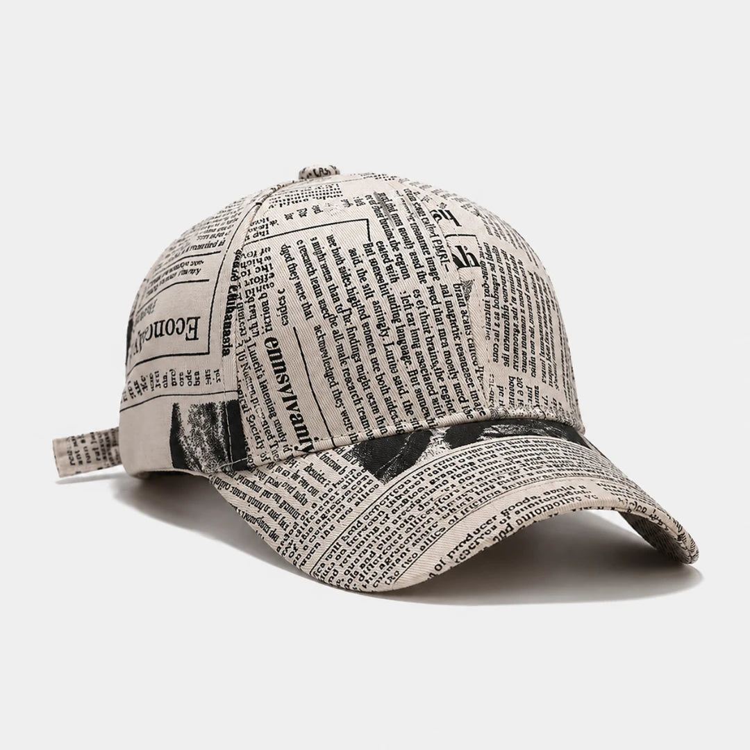 Josh & Tate - InkPress™ Newsprint Cap - A baseball cap printed with a newspaper clippings pattern in black ink on a light beige fabric, shown on a light gray background.