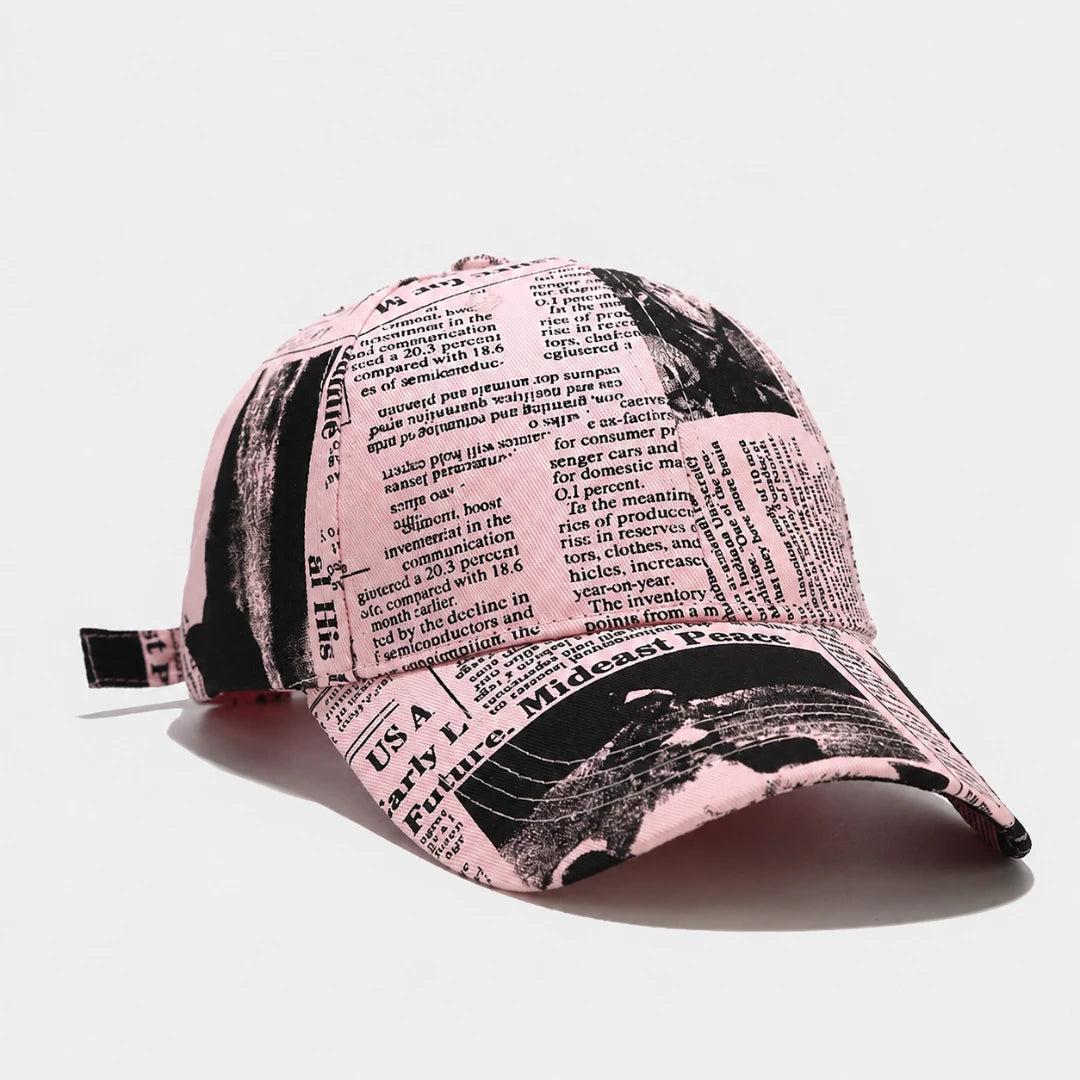 Josh & Tate - InkPress™ Newsprint Cap - A baseball cap featuring a pink and black newspaper print pattern, photographed from an elevated angle on a light gray background.