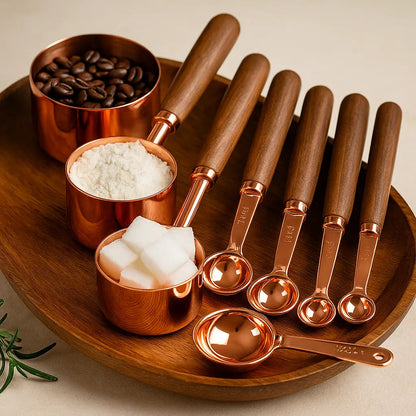 Set of copper measuring spoons with wooden handles on a wooden tray with ingredients.