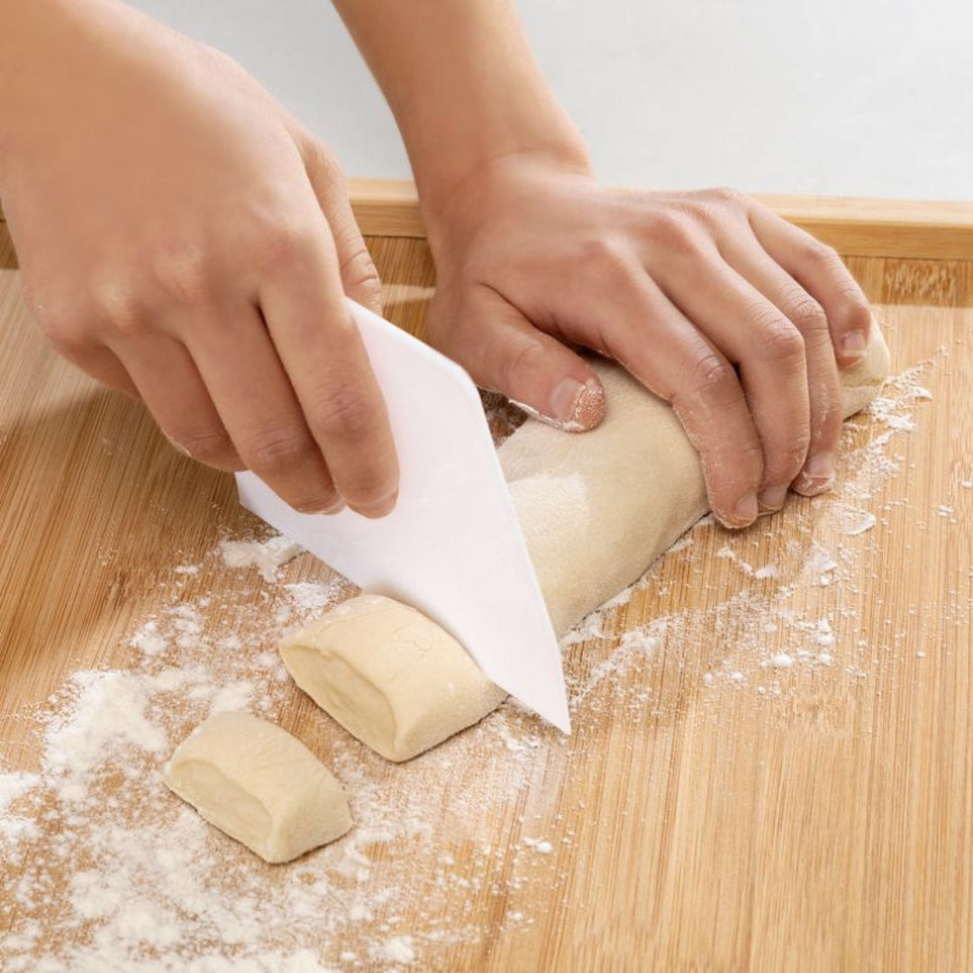 Hands cutting dough with a knife on a wooden surface