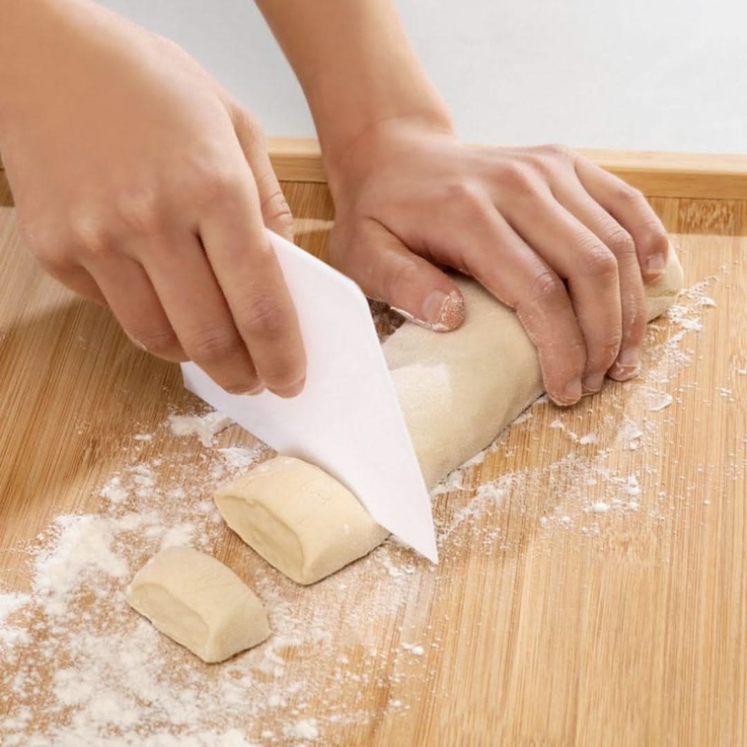 Hands cutting dough with a knife on a wooden surface