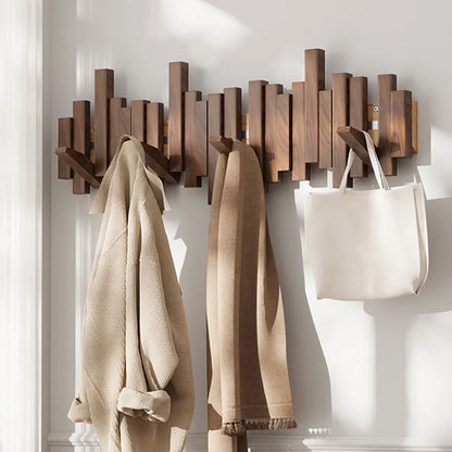 Wooden wall-mounted coat rack with hooks holding a coat, scarf, and bag against a white wall.