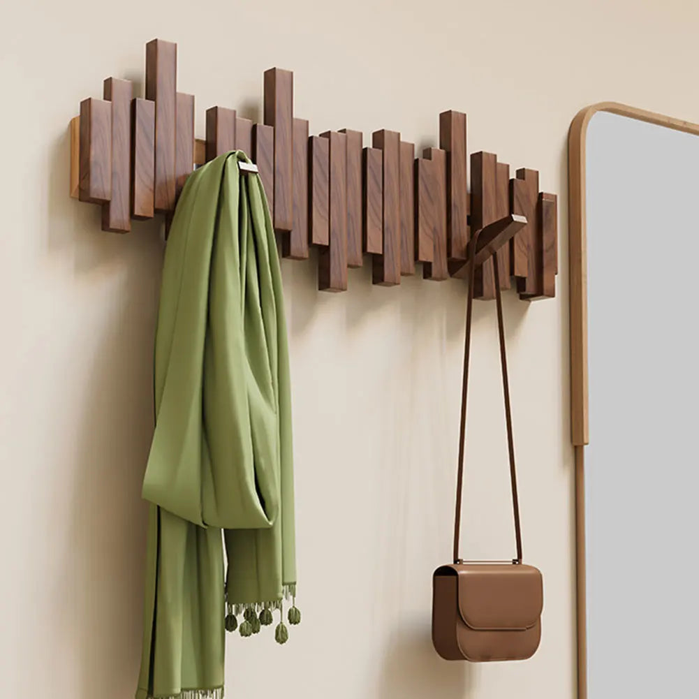 Wooden wall hook with green scarf and brown handbag on a beige wall.