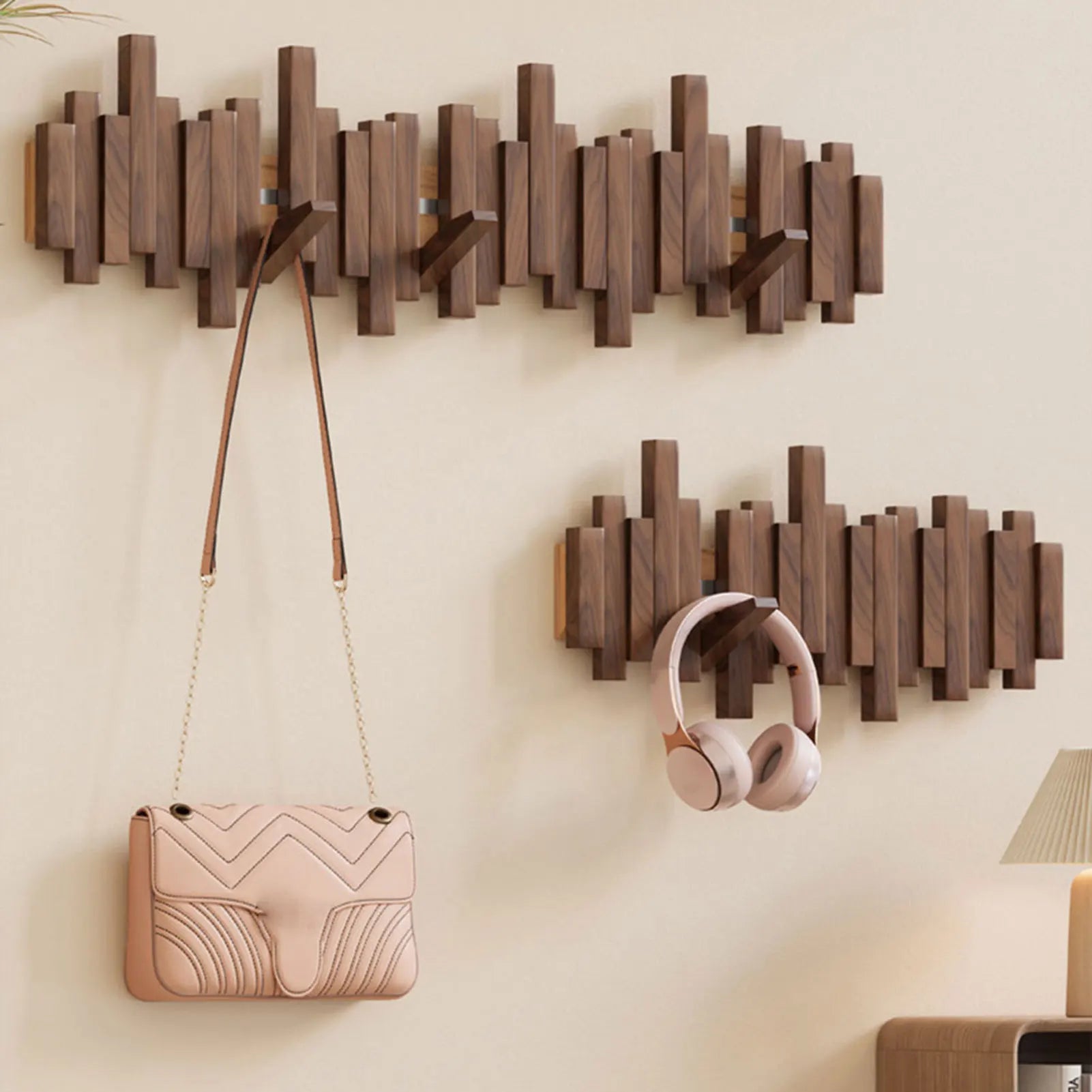 Wooden wall hooks holding a handbag and headphones against a beige wall.