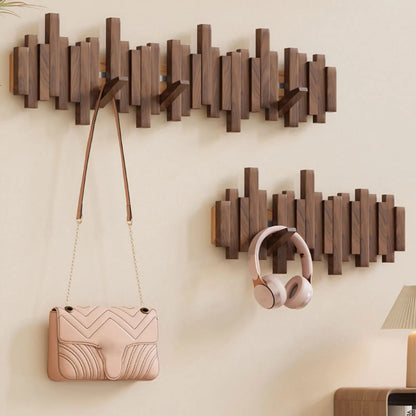Wooden wall hooks holding a handbag and headphones against a beige wall.