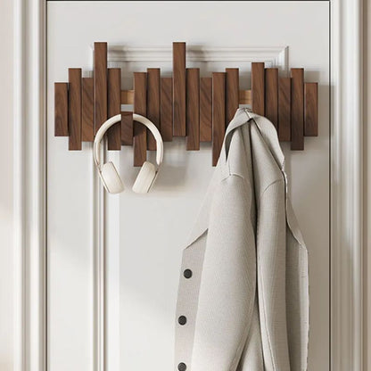 Wooden wall-mounted coat rack with a coat and headphones hanging on it against a white wall.