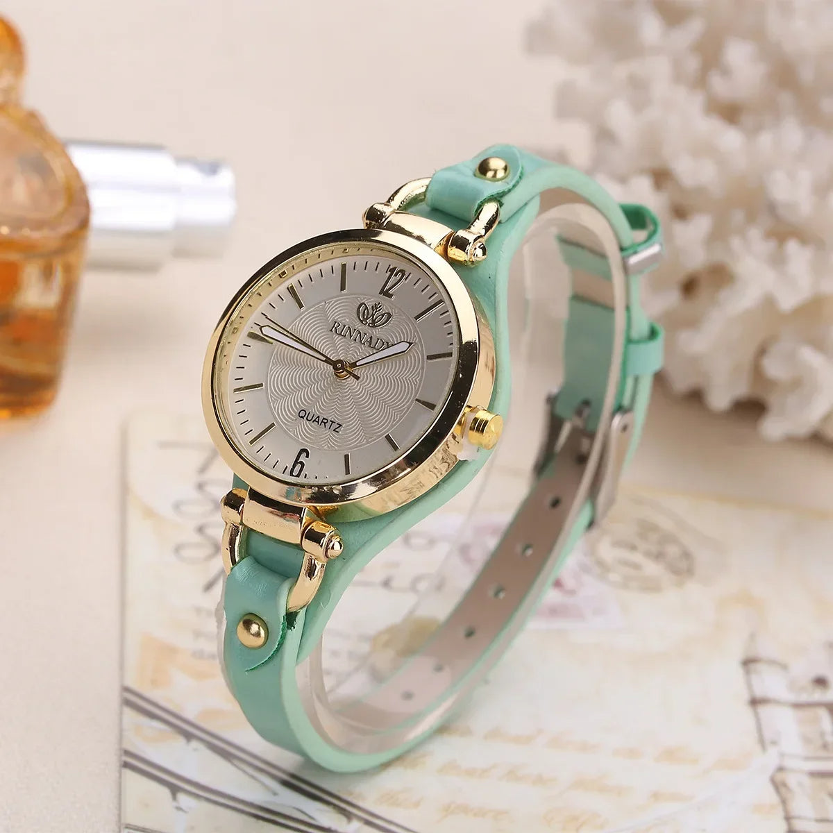 Mint green watch with gold accents on a surface with a blurred background